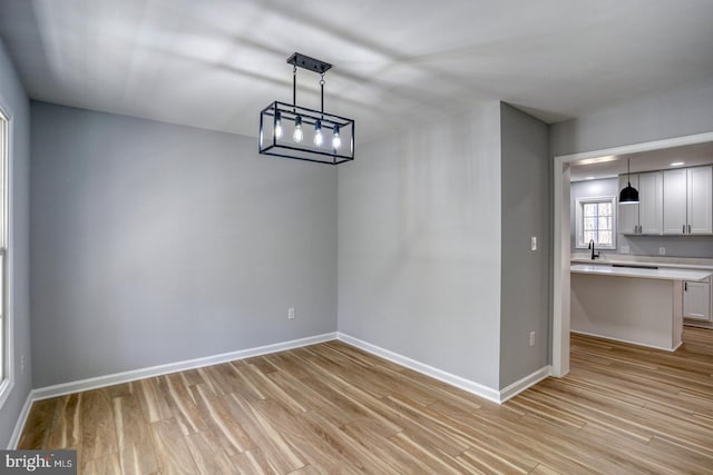 unfurnished dining area featuring a sink, baseboards, and light wood-style flooring