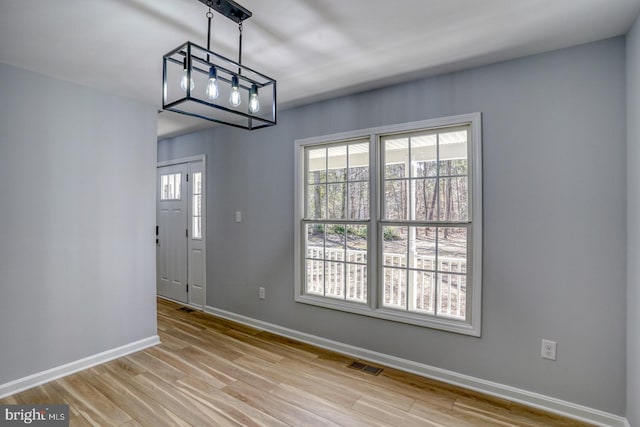 unfurnished dining area featuring light wood-type flooring, visible vents, and baseboards