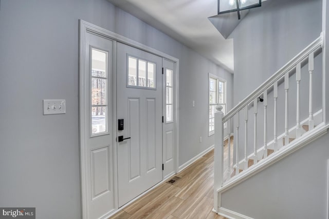 foyer with stairs, visible vents, wood finished floors, and baseboards