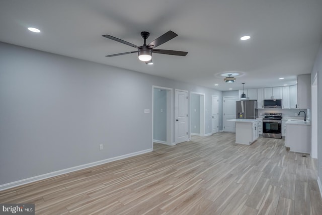 unfurnished living room with baseboards, recessed lighting, ceiling fan, a sink, and light wood-type flooring