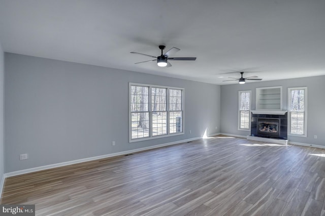 unfurnished living room featuring baseboards, a healthy amount of sunlight, wood finished floors, and a tiled fireplace