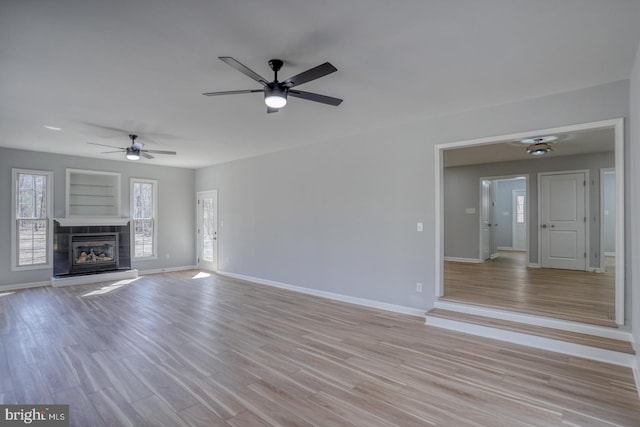 unfurnished living room with light wood finished floors, a fireplace, a ceiling fan, and baseboards