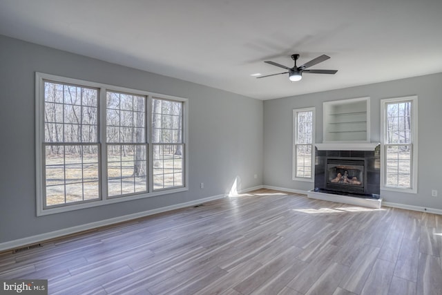 unfurnished living room featuring visible vents, ceiling fan, baseboards, a tiled fireplace, and wood finished floors