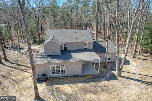 rear view of house with dirt driveway, a forest view, cooling unit, a shingled roof, and a carport