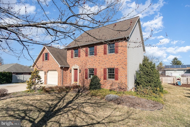 colonial home featuring brick siding, a front lawn, fence, a garage, and driveway