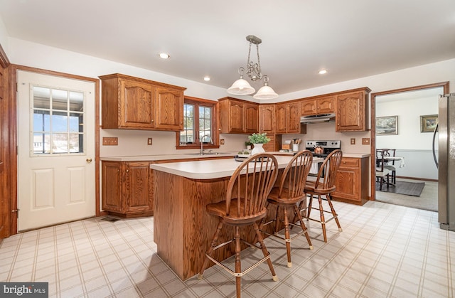 kitchen with light floors, a sink, light countertops, under cabinet range hood, and brown cabinets