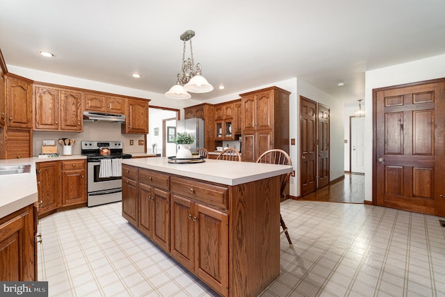 kitchen featuring a center island, under cabinet range hood, light floors, brown cabinets, and stainless steel appliances