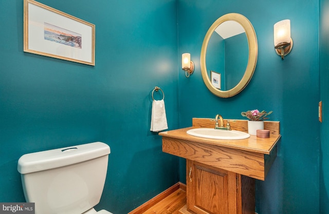 bathroom with toilet, wood finished floors, baseboards, and a sink