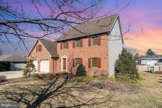 colonial house featuring a garage, brick siding, concrete driveway, and fence