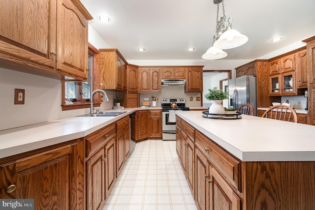 kitchen with brown cabinetry, a sink, stainless steel appliances, under cabinet range hood, and a center island