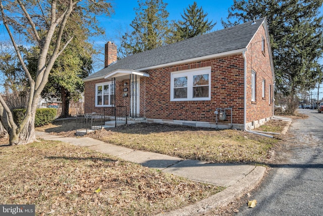 bungalow with brick siding, a chimney, and a shingled roof