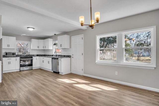 kitchen with baseboards, appliances with stainless steel finishes, white cabinetry, dark countertops, and a chandelier