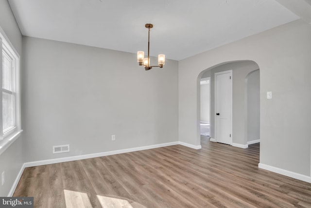 unfurnished room featuring wood finished floors, arched walkways, visible vents, and baseboards