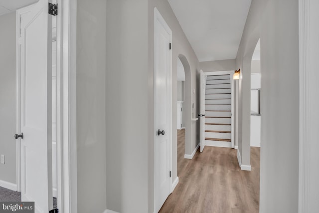 hallway with stairs, light wood-style flooring, baseboards, and arched walkways