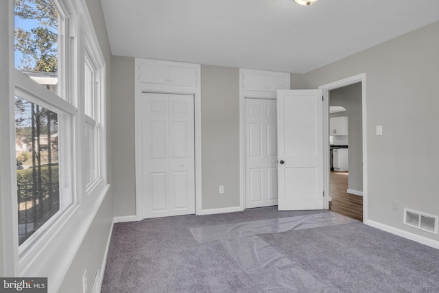 unfurnished bedroom featuring visible vents, baseboards, arched walkways, and carpet flooring