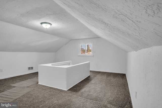 additional living space with baseboards, dark carpet, a textured ceiling, and lofted ceiling