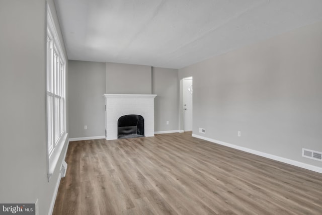 unfurnished living room with visible vents, a fireplace, baseboards, and wood finished floors