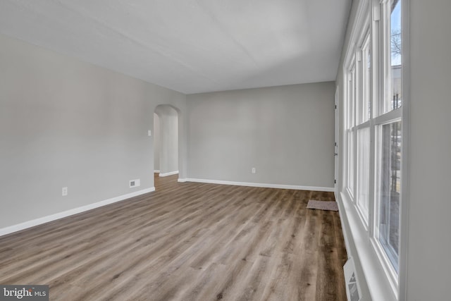 spare room with baseboards, arched walkways, and wood finished floors