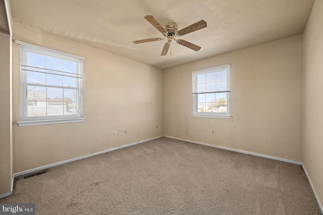 carpeted empty room with visible vents, a healthy amount of sunlight, baseboards, and ceiling fan