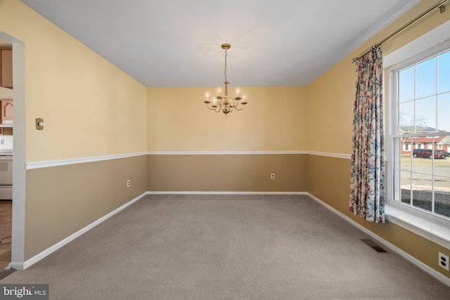 carpeted spare room featuring a wealth of natural light, visible vents, baseboards, and a notable chandelier