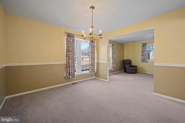 carpeted empty room featuring baseboards, visible vents, and a chandelier