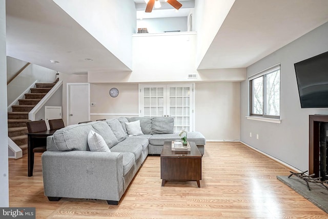 living room featuring light wood finished floors, visible vents, stairs, a towering ceiling, and a ceiling fan