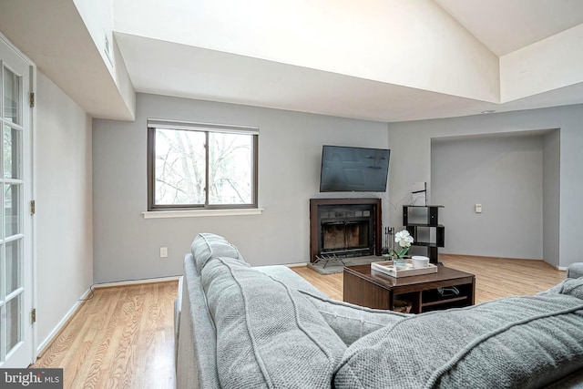 living room with lofted ceiling, a fireplace with flush hearth, wood finished floors, and baseboards