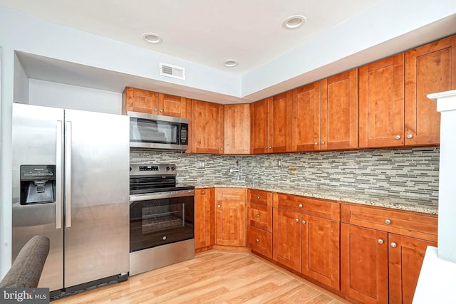 kitchen with visible vents, light stone countertops, decorative backsplash, brown cabinets, and stainless steel appliances