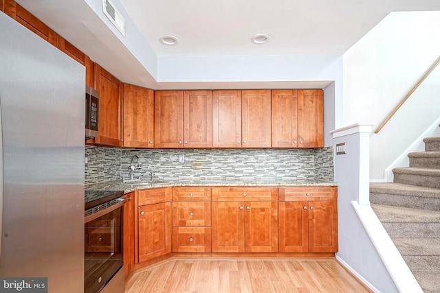 kitchen featuring visible vents, brown cabinets, light wood-style flooring, light stone counters, and appliances with stainless steel finishes