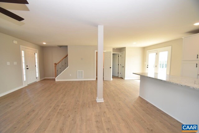 unfurnished living room featuring stairs, light wood-style flooring, baseboards, and visible vents