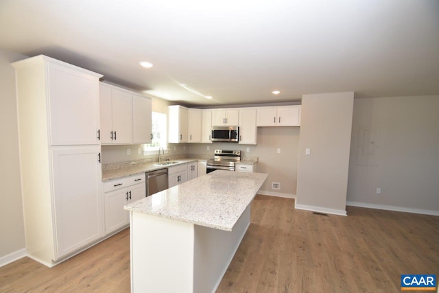 kitchen with light wood finished floors, a kitchen island, a sink, stainless steel appliances, and white cabinetry