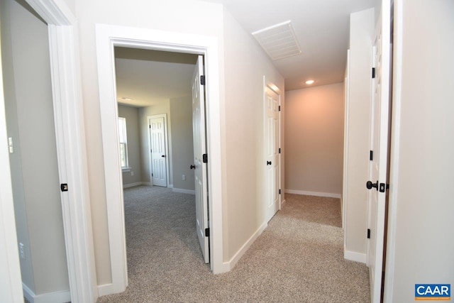 hallway featuring visible vents, light carpet, and baseboards