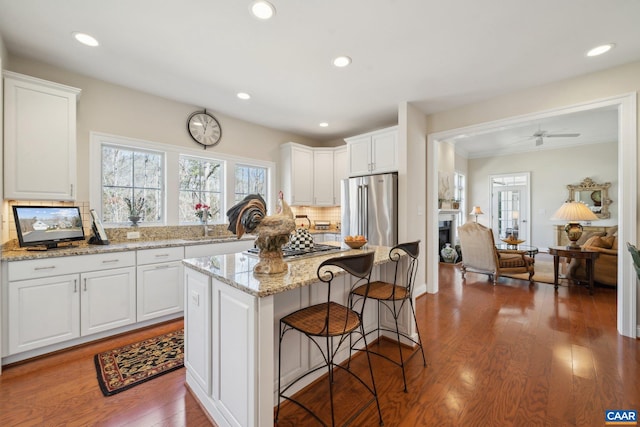 kitchen with light stone countertops, a kitchen bar, stainless steel appliances, wood finished floors, and white cabinetry