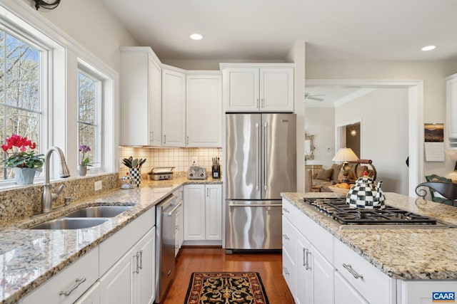 kitchen with a sink, backsplash, dark wood finished floors, stainless steel appliances, and white cabinets