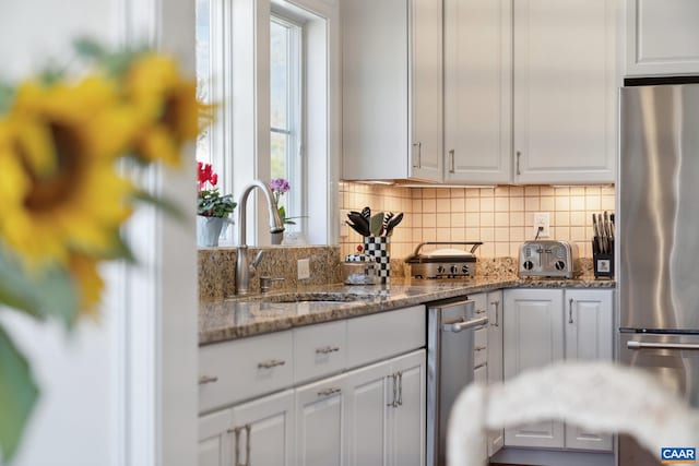 kitchen featuring backsplash, white cabinetry, freestanding refrigerator, and a sink