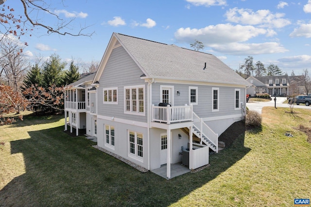 back of house featuring a deck, a yard, roof with shingles, a sunroom, and stairs