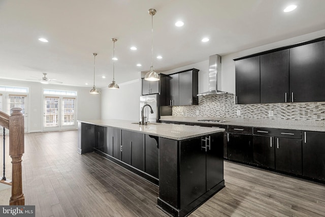 kitchen featuring a spacious island, wood finished floors, dark cabinetry, and wall chimney exhaust hood