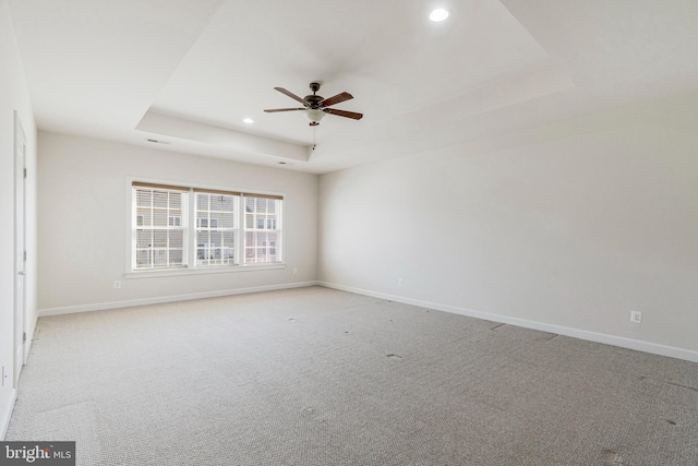 spare room with a tray ceiling, baseboards, and light carpet