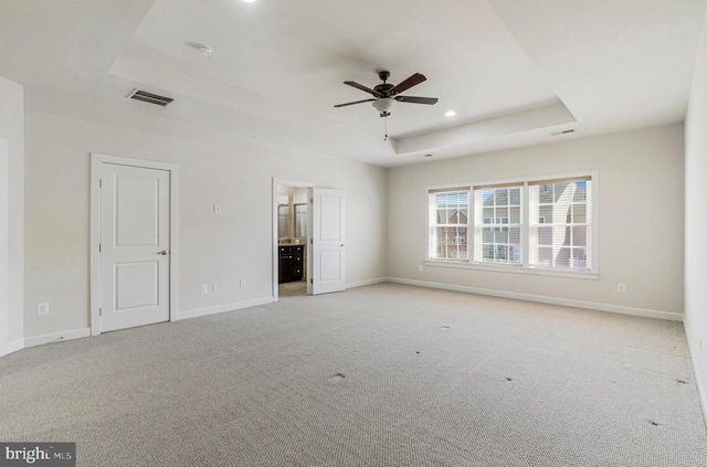 unfurnished bedroom with light carpet, visible vents, a raised ceiling, and baseboards