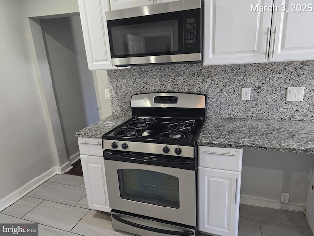 kitchen with tasteful backsplash, baseboards, dark stone counters, appliances with stainless steel finishes, and white cabinetry