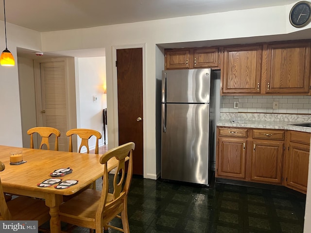 kitchen featuring freestanding refrigerator, light countertops, dark floors, brown cabinets, and backsplash