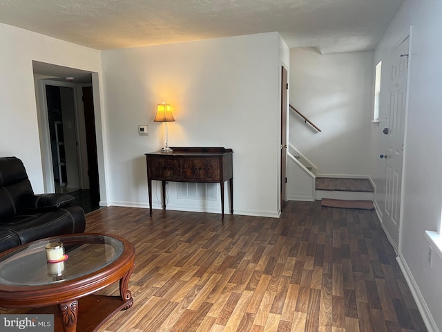 living room featuring stairway, a textured ceiling, baseboards, and wood finished floors