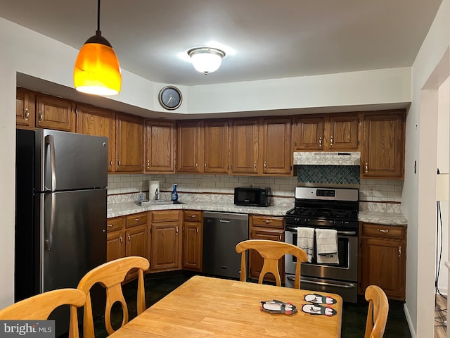 kitchen with brown cabinets, under cabinet range hood, appliances with stainless steel finishes, light countertops, and decorative backsplash