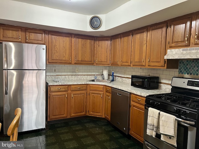 kitchen with dark floors, under cabinet range hood, light countertops, appliances with stainless steel finishes, and a sink