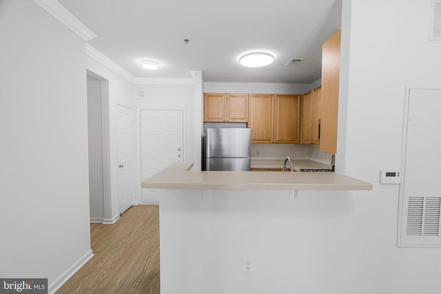 kitchen with visible vents, freestanding refrigerator, a peninsula, light wood finished floors, and light countertops