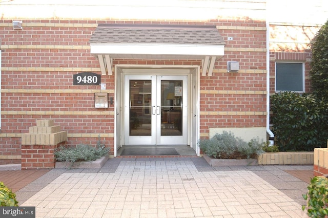 view of exterior entry featuring french doors, brick siding, and roof with shingles