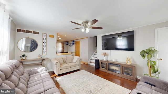 living room with stairway, baseboards, visible vents, dark wood-style flooring, and ceiling fan