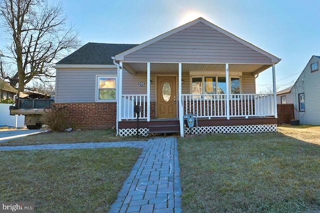 bungalow-style house featuring brick siding, covered porch, a shingled roof, and a front lawn