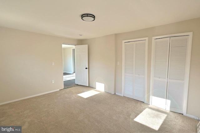 unfurnished bedroom featuring baseboards, two closets, and carpet