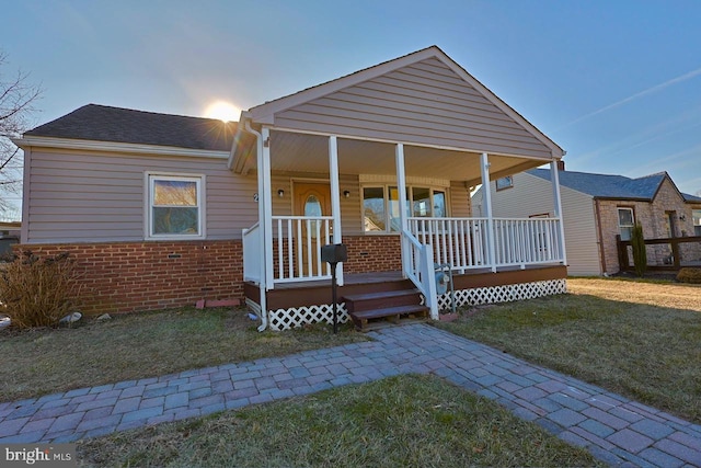 view of front facade with a porch, brick siding, and a front lawn